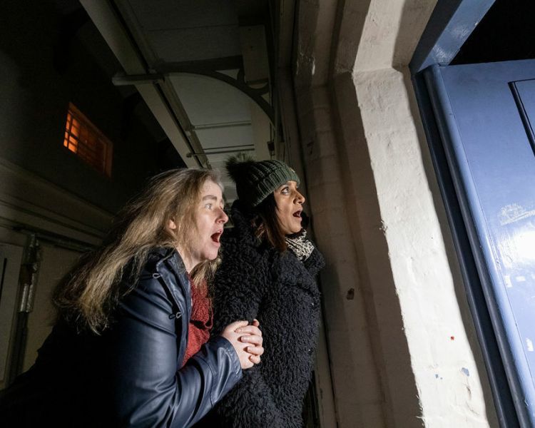 two people looking into a prison cell at night on a ghost tour experience at a haunted prison experience day