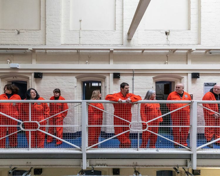 people in orange overalls standing on the balcony in a prison as part of a prison break experience day