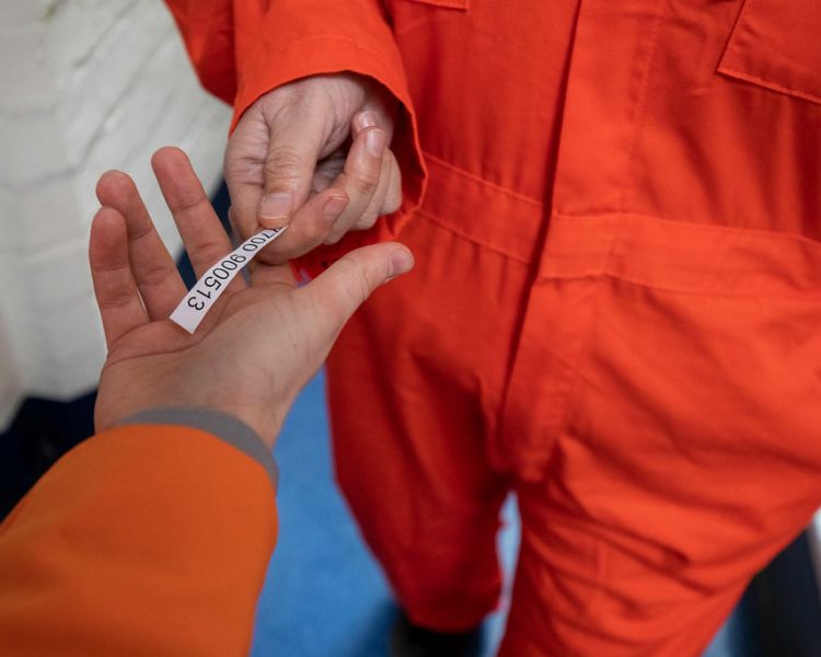person in orange overalls handing over a small piece of paper with a code on to another person as part of a prison break experience day