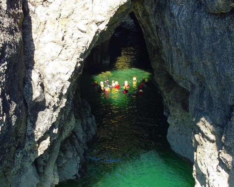 People swimming in sea cave on coasteering experience in pembrokeshire