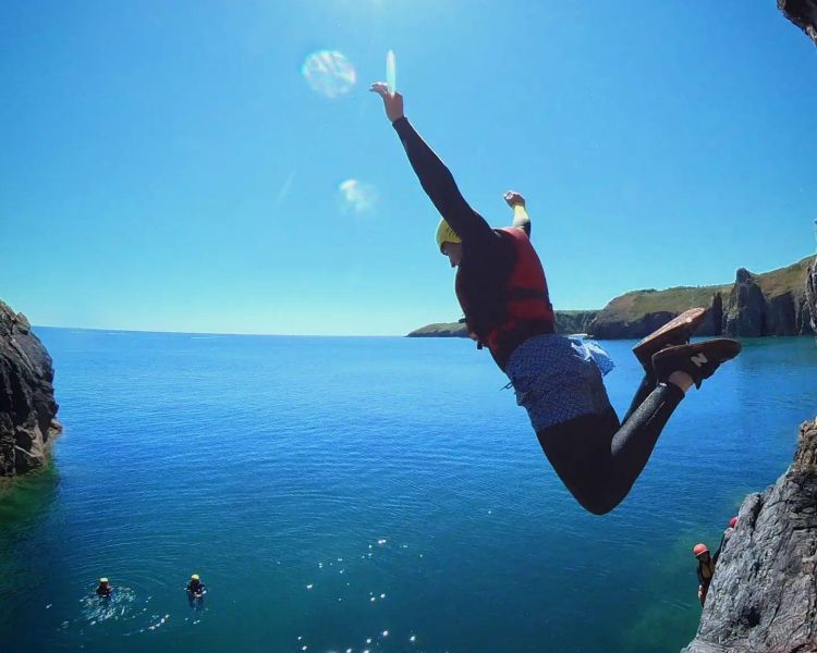 Person jumping off a cliff on coasteering experience in pembrokeshire