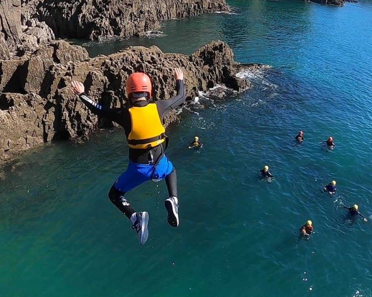Person jumping off cliff into sea on coasteering experience in pembrokeshire