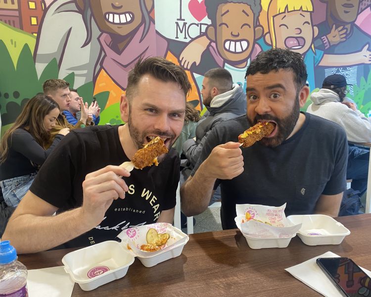 Two men eating corndogs on manchester food tour