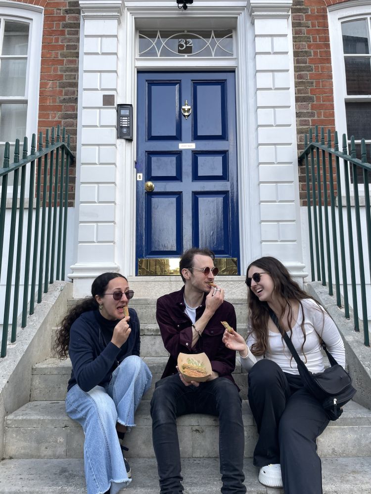 Three people sitting on steps eating on a mystery food tour in london
