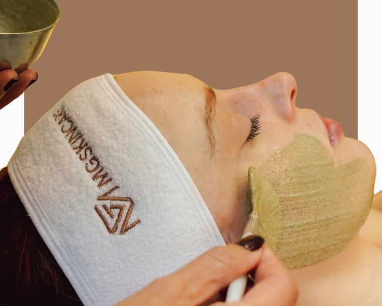 Applying a green face peel to womans face for facial