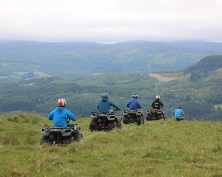 people riding quad bikes over a hill surrounded by countryside