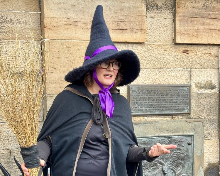 guide next to plaque on wall on a witches walking tour in edinburgh