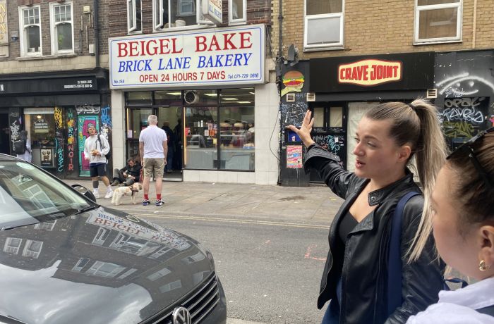 Guide pointing to beigel bake shop on east end london food tour