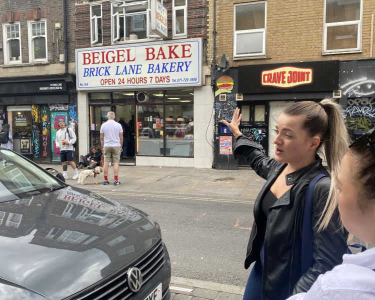 Guide pointing to beigel bake shop on east end london food tour
