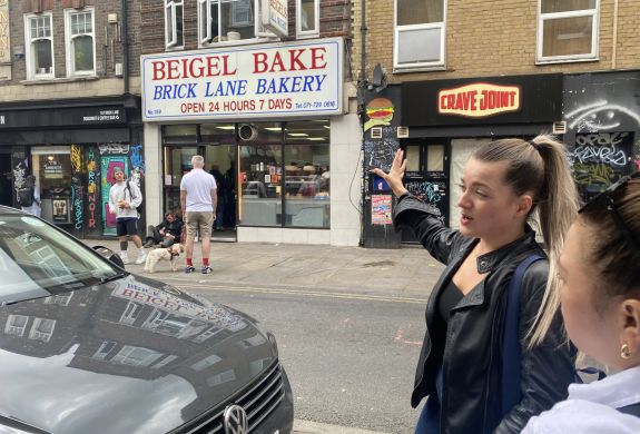 Guide pointing to beigel bake shop on east end london food tour