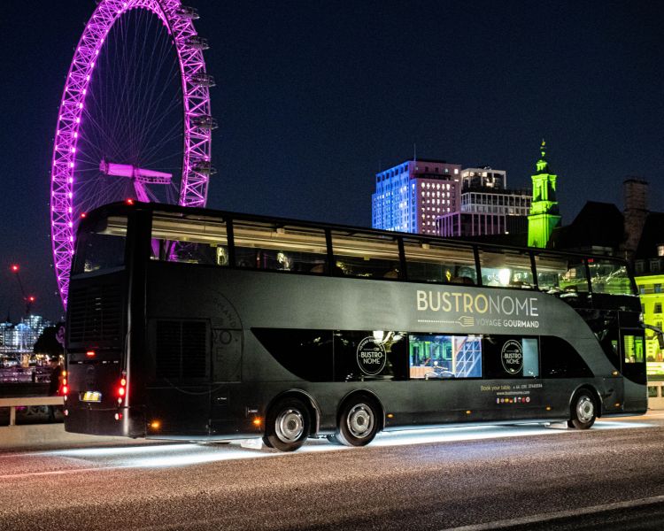 The bustronome london dining bus crossing bridge with london eye lit pink in background