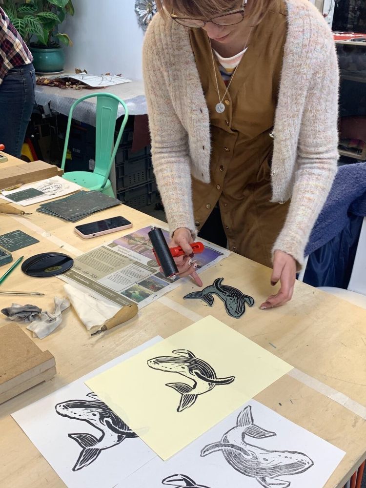 lady rolling paint onto lino to print a design at a craft workshop