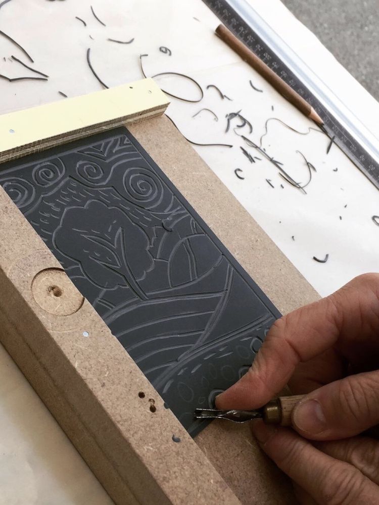 person cutting a design into a piece of lino on a craft workshop