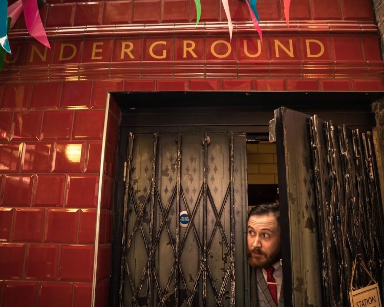 man peaking from behind door at cahoots underground 1940s style bar in london