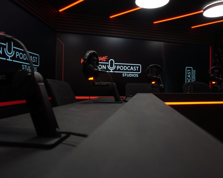 the desks in a podcast studio with tv wall behind