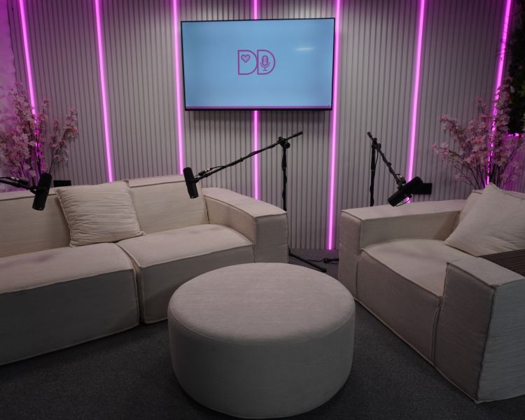 white podcast studio in exeter with comfy chairs and microphones and tv on wall