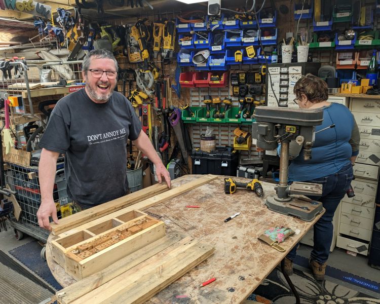 man in workshop making a bug house from wood offcuts