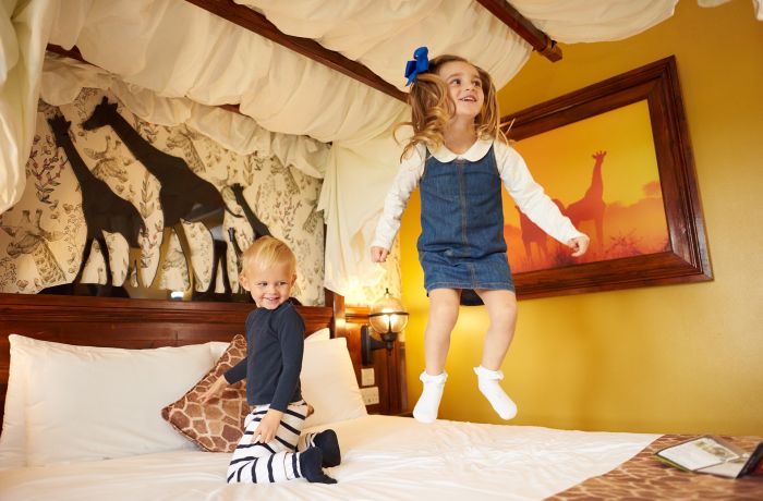 two young kids bouncing on bed in the giraffe room at the safari hotel at chessington world of adventures