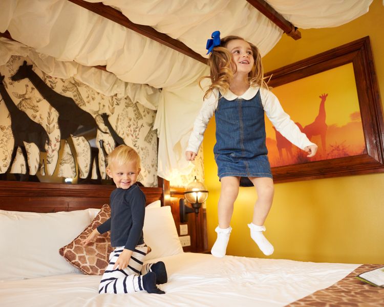two young kids bouncing on bed in the giraffe room at the safari hotel at chessington world of adventures