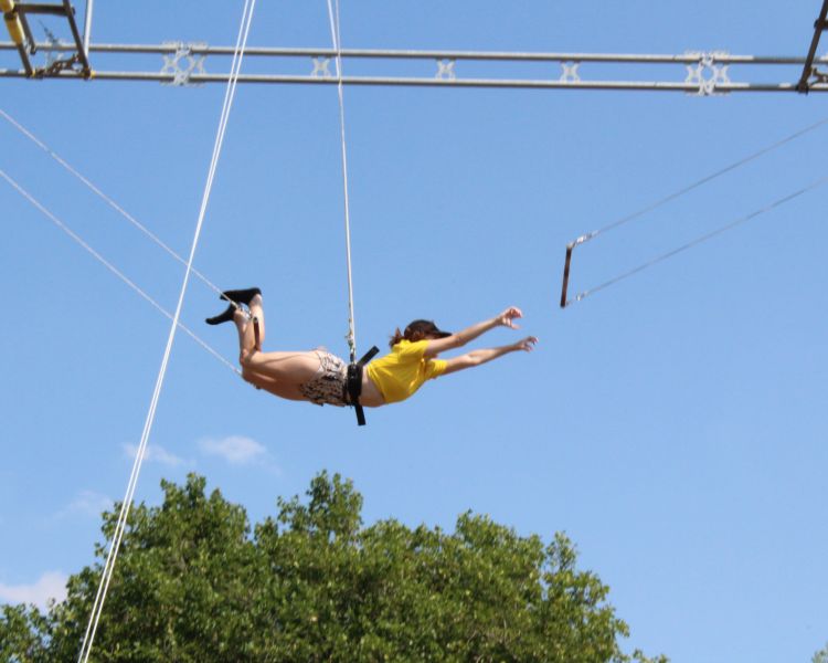 A lady mid air transferring on a trapeze