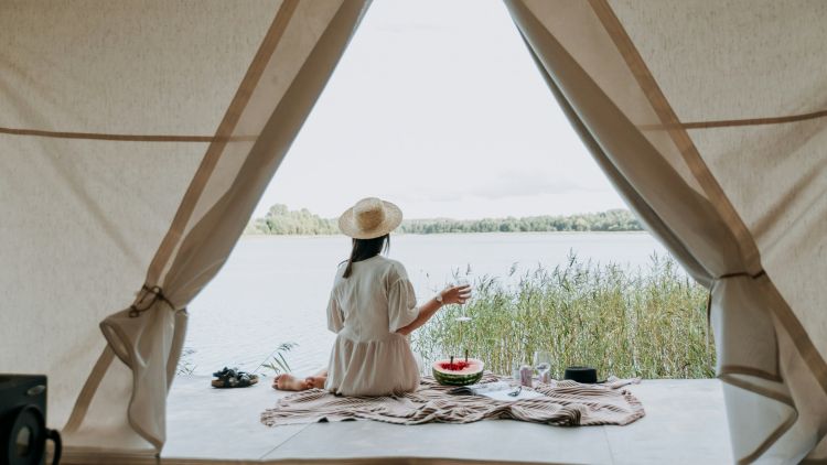 Stock image of woman sitting in entrance of glamping tent overlooking lake