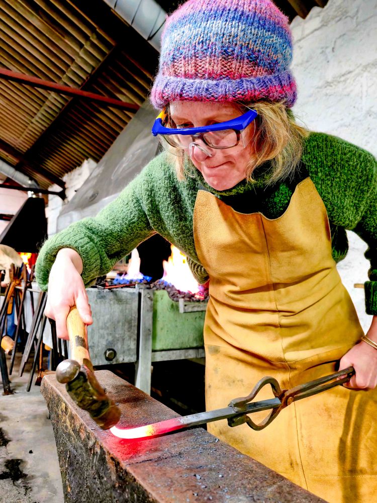 Woman shaping metal into hook on blacksmith experience