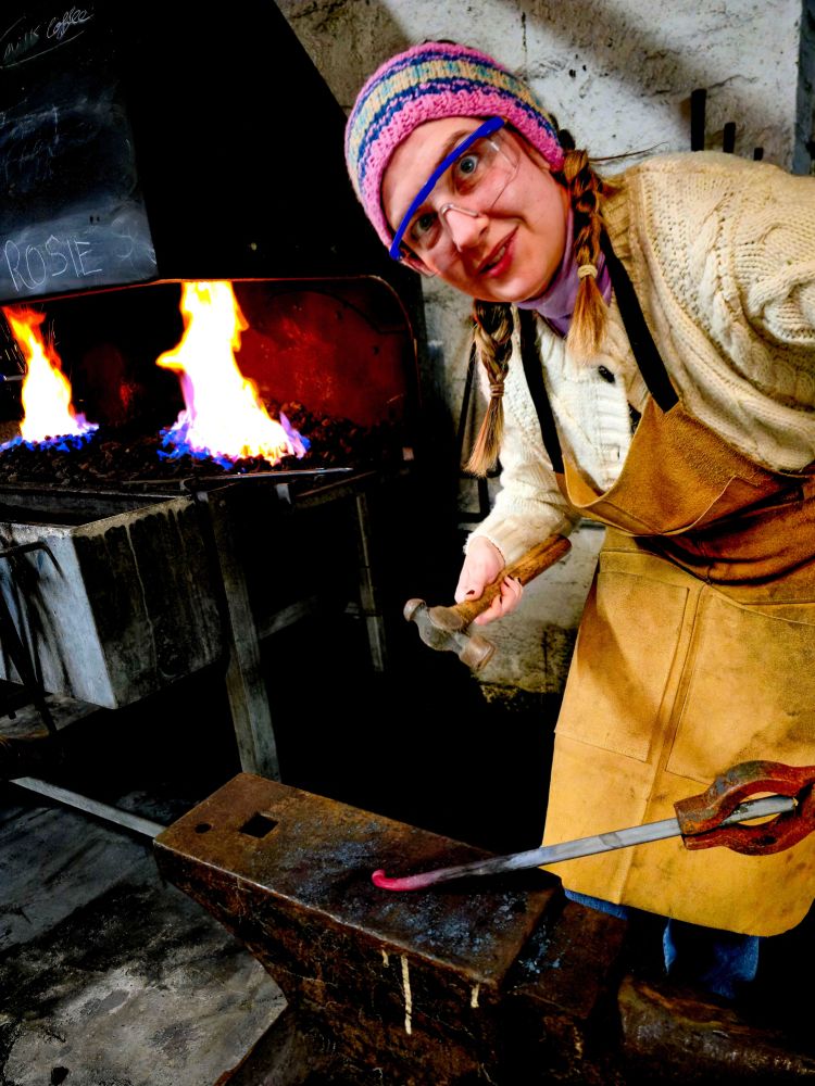 Woman shaping metal into hook with hammer on blacksmith experience