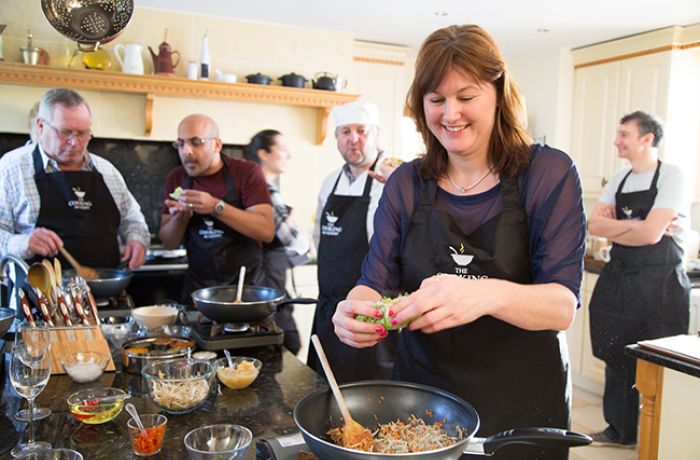 people being taught a cookery lesson in a kitchen with the help of professional chefs on a cookery course experience day