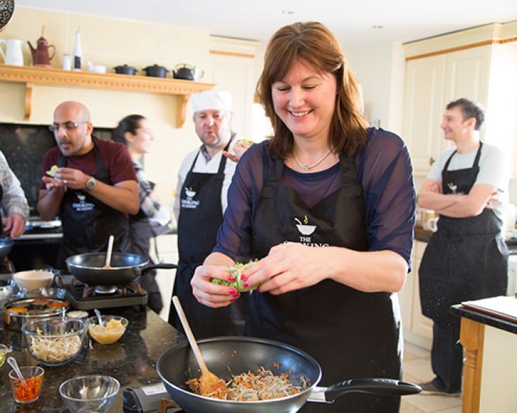 people being taught a cookery lesson in a kitchen with the help of professional chefs on a cookery course experience day
