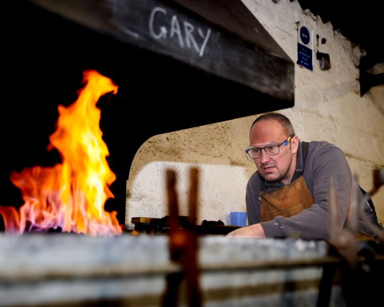 man using forge to heat up metal on a blacksmith day experience