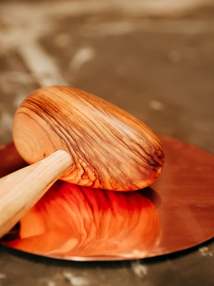 a wooden hammer and a round sheet of copper for making a bowl on a silversmith experience