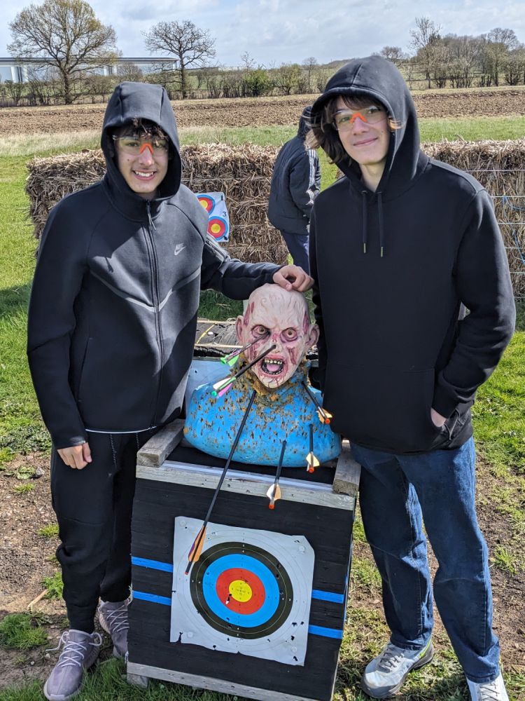 two teenage boys next to zombie head target full of arrows on a zombie apocalypse weapons training experience