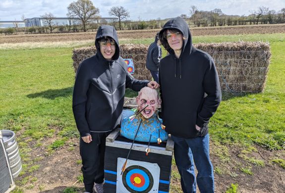 two teenage boys next to zombie head target full of arrows on a zombie apocalypse weapons training experience