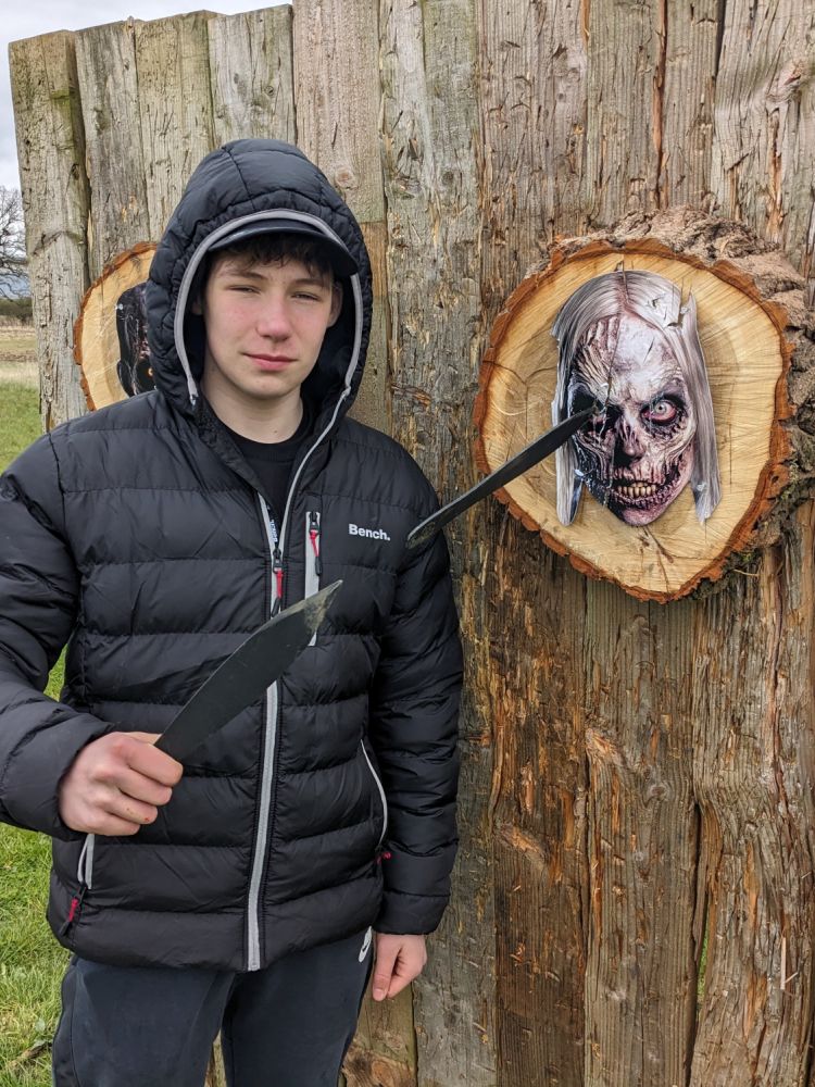 teenage boy next to zombie head target with knife stuck in it