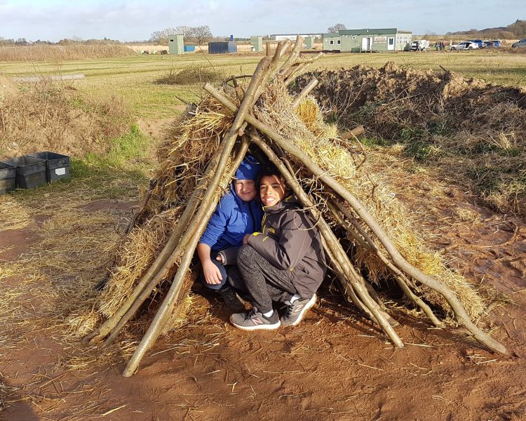 two people inside a den made of sticks on a bushcraft experience