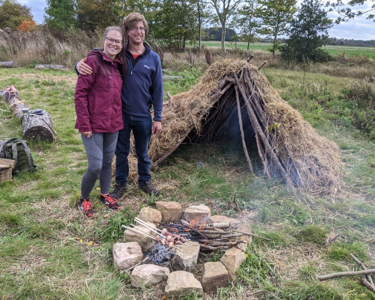 couple next to a campfire and den made on a bushcraft experience