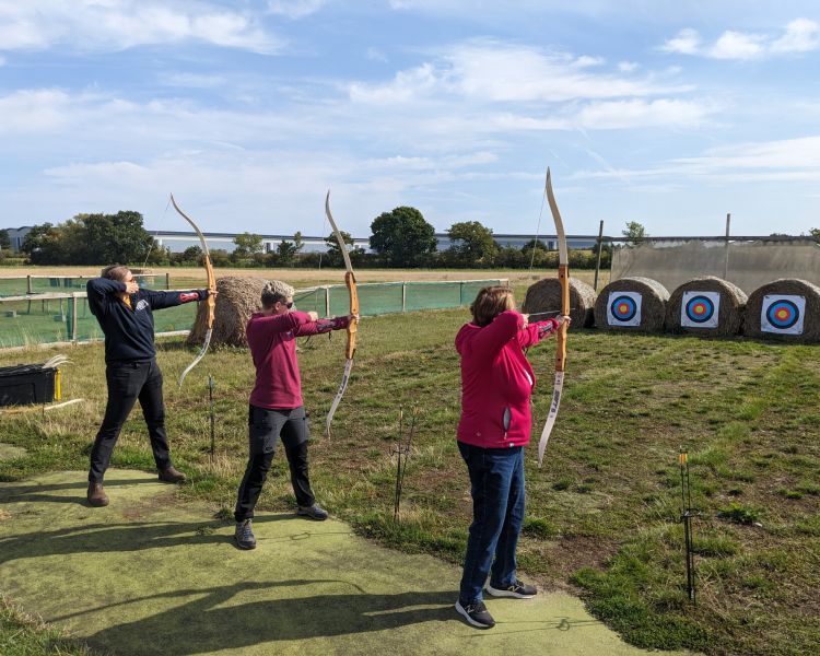 three people shooting arrows at targets on a robin hood weapons experience