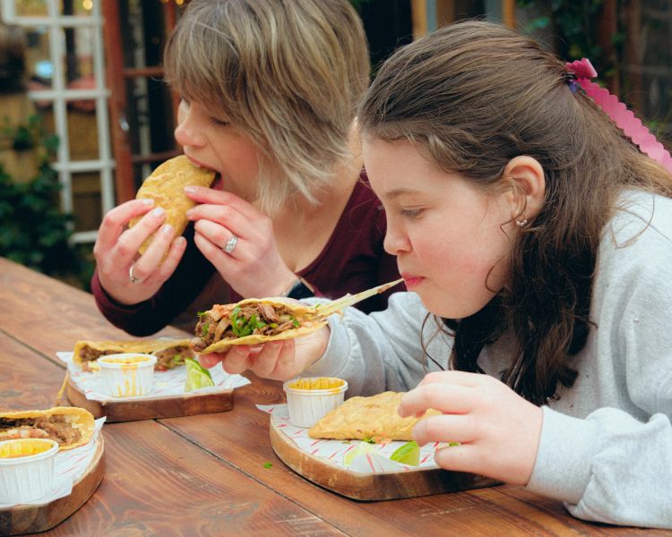 Woman and daughter eating tacos on food treasure hunt in manchester