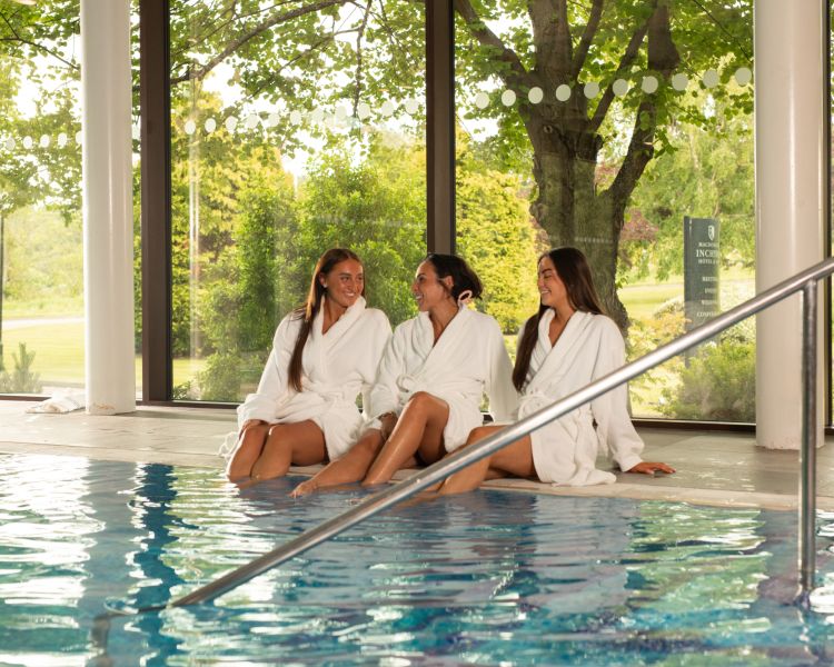 Three women lounging by a pool in spa robes