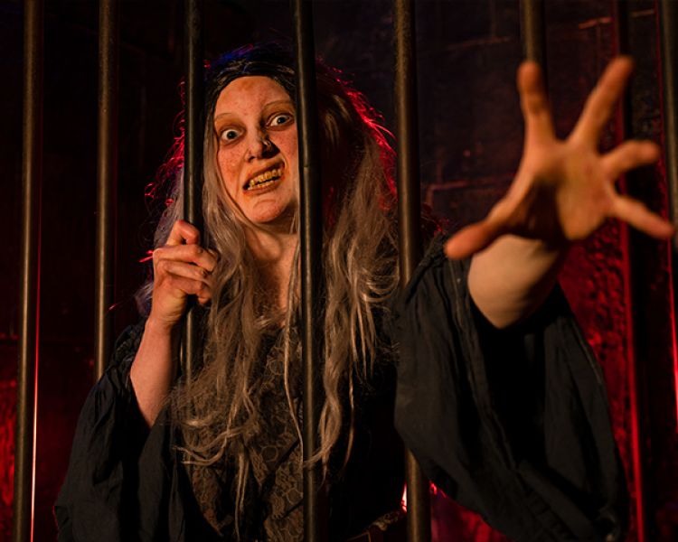 actor dressed in costume reaching out from behind bars as part of the london dungeon experience