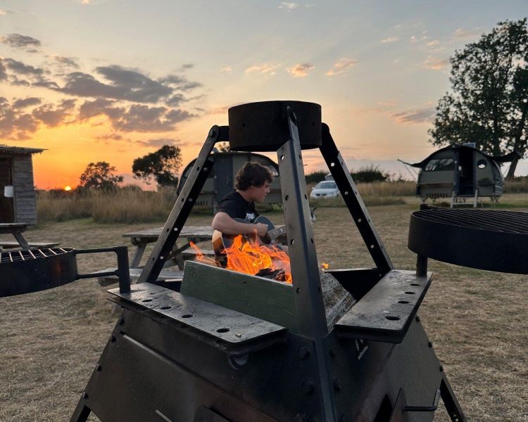 man playing guitar next to campfire on glamping site