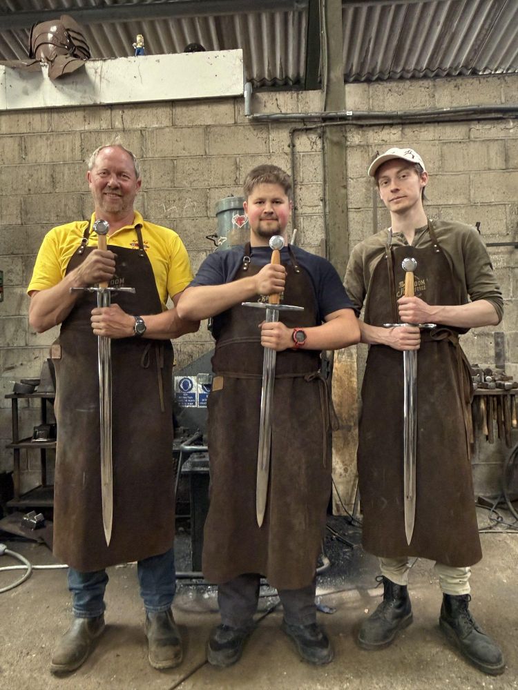 three men holding the swords they made on a sword making blacksmith experience