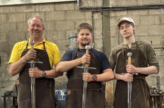 three men holding the swords they made on a sword making blacksmith experience