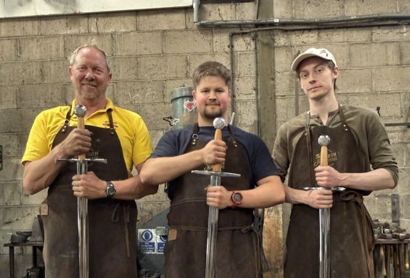 three men holding the swords they made on a sword making blacksmith experience