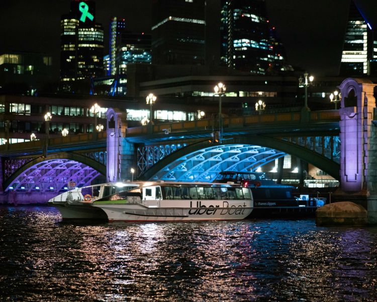 uber boat passing under bridge lit up in blue and purple