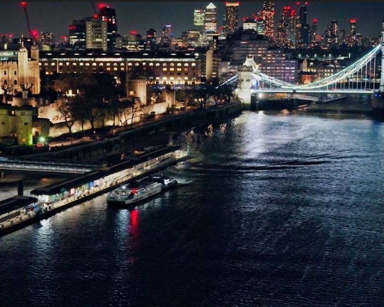 uber boat at tower pier at night with london skyline lit up
