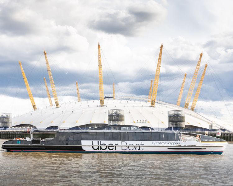 an uber boat passing the o2 arena on the river thames