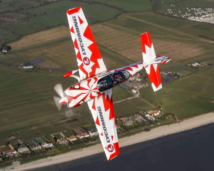 red and white plane on its side in the air on an aerobatic flying experience
