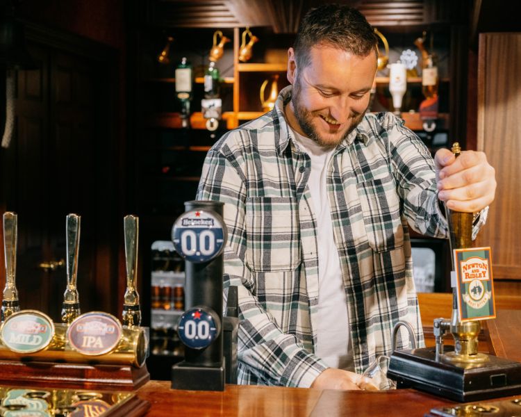 A fan pulls a pint behind the replica Rovers bar located in the Coronation Street Experience