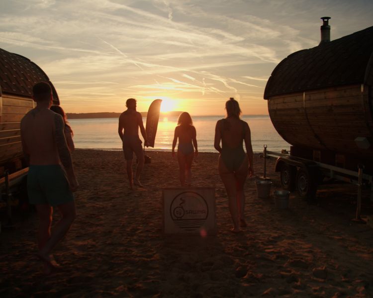 people walking out of sauna pods on beach at sunset in wales